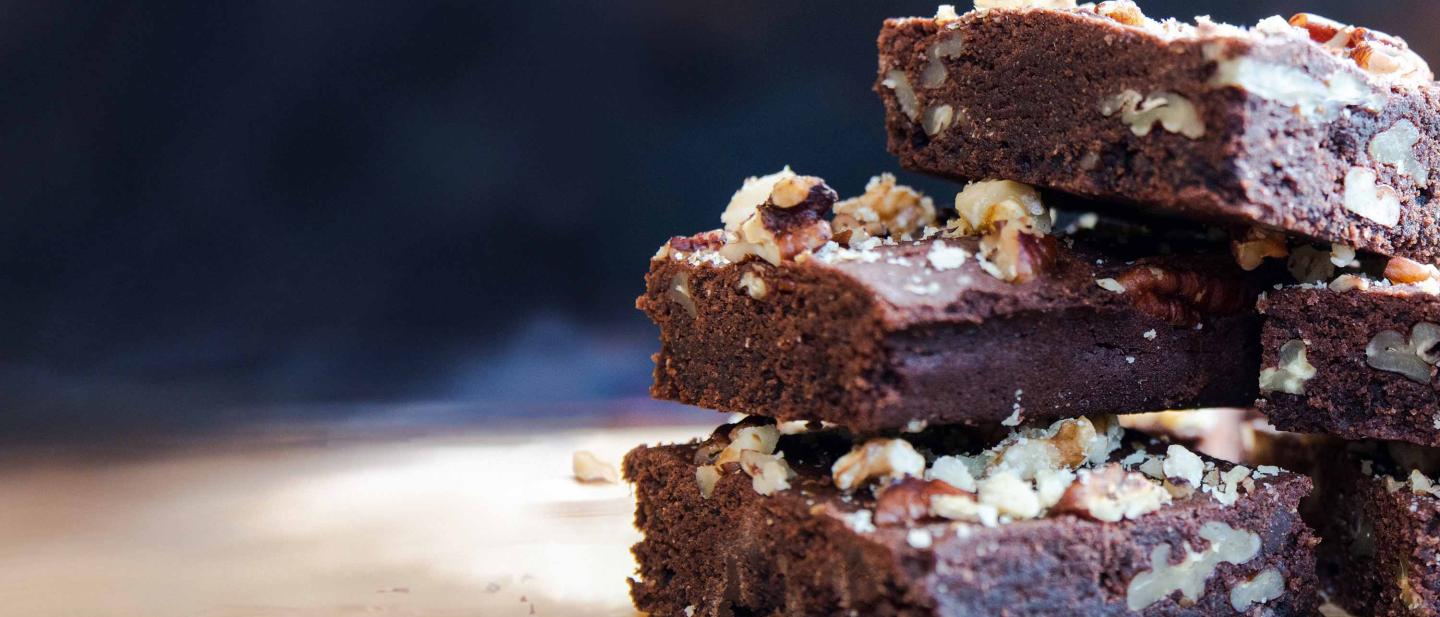 A stack of chocolate and pecan brownies, sprinkled with pecan crumbs and crushed walnut, fresh out of the oven